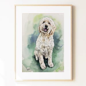 May include: A framed watercolor painting of a cream-colored Goldendoodle dog with a curly coat, sitting and facing forward with an open mouth. The background features blended washes of green and blue, with a signature in the bottom left corner.