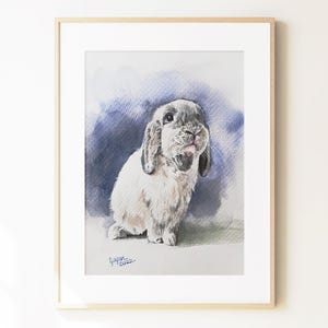 May include: A framed watercolor painting of a lop-eared rabbit with light gray and white fur. The rabbit is positioned against a dark blue and purple wash background. The artist signature and the year 2022 are visible in the bottom left corner.