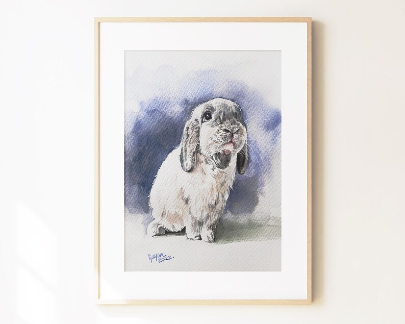 May include: A framed watercolor painting of a lop-eared rabbit with light gray and white fur. The rabbit is positioned against a dark blue and purple wash background. The artist signature and the year 2022 are visible in the bottom left corner.