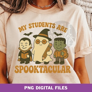 Puede incluir: Camiseta beige con un diseño temático de Halloween. El diseño presenta personajes de dibujos animados de un vampiro, un fantasma y el monstruo de Frankenstein, con el texto "MY STUDENTS ARE SPOOKTACULAR". Dos murciélagos negros están encima de los personajes.