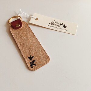 May include: A brown leather keychain with a gold key ring and a small image of three birds. The keychain has the text "twin sparrow" and "twinsparrow.com" printed on it.