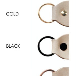May include: Keyring metal colors: gold, black, and rose gold. Each keyring features a leather strap with a metal ring and a small metal button.