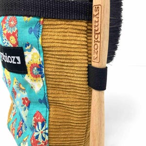 May include: A climbing chalk bag with a floral pattern and a wooden brush. The chalk bag is made of corduroy and has a black strap. The brush has the word "Symbiozy" printed on it.