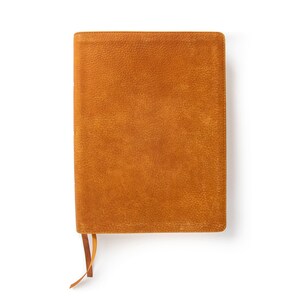 Op de afbeelding: Een bruin lederen gebonden dagboek met een lint-bladwijzer. Het dagboek heeft een gestructureerd oppervlak en een eenvoudig ontwerp.