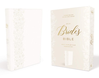 Puede incluir: Una Biblia encuadernada en cuero blanco con letras doradas que dicen "Biblia de la Novia" y "La Palabra de Dios para tu día de boda". La portada presenta un diseño floral con detalles dorados.