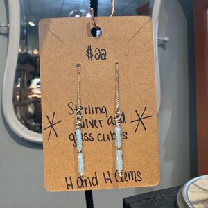 May include: Sterling silver earrings with light blue glass cubes. The earrings hang from a silver chain. The tag reads "Sterling silver and glass cubes" and "H and H Gems".
