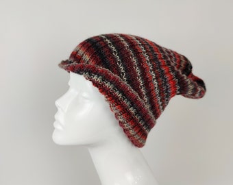 May include: A knitted beanie hat in a mix of red, black, and beige stripes. The hat has a brim and is displayed on a white mannequin head. The hat's texture is visible, suggesting a handmade or artisanal quality. The hat is a winter accessory.