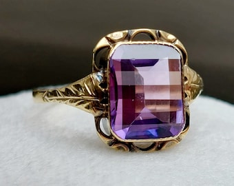 Può includere: Un anello vintage in oro con una grande ametista rettangolare. L'anello presenta un design a filigrana ornato con accenti di foglie sulle spalle. L'ametista mostra sfumature di viola ed è incastonata in una lunetta dettagliata.