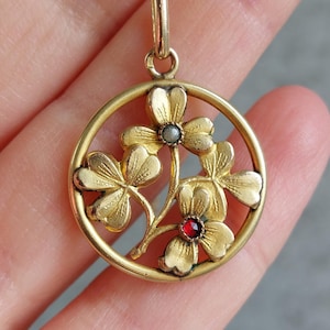 Könnte beinhalten: Eine goldene Halskette mit einem Anhänger in Form eines Kreises, der mit vier Kleeblättern und einem roten und weißen Edelstein in der Mitte verziert ist.