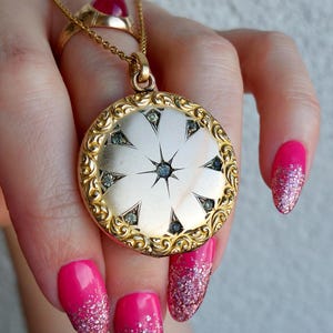 Könnte beinhalten: Eine goldfarbene Halskette mit einem Medaillon im Sternmuster und kleinen Edelsteinen. Das runde Medaillon hat einen verzierten, filigranen Rand. Ein goldener Ring mit einem roten Stein ist ebenfalls sichtbar.