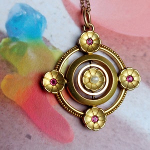 May include: A gold pendant necklace with a circular design featuring four flower-shaped accents with pink gemstones. The center of the pendant has a pearl.