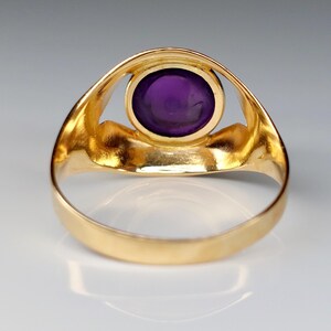 May include: A gold ring featuring a large, oval, deep purple gemstone. The ring's band and setting are a bright, polished gold. The gemstone is the focal point, set in a simple, elegant design.