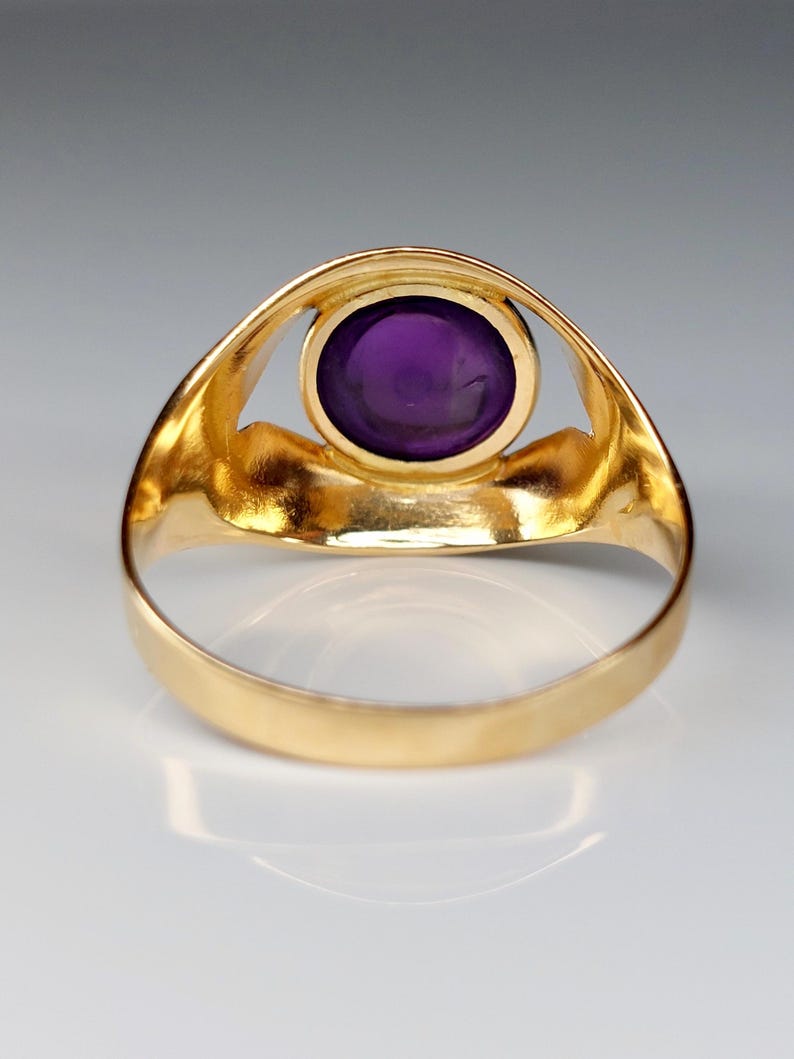 May include: A gold ring featuring a large, oval, deep purple gemstone. The ring's band and setting are a bright, polished gold. The gemstone is the focal point, set in a simple, elegant design.
