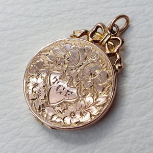 May include: A gold locket with an engraved floral design and a heart with the initials "W.G." inside. The locket has a bow-shaped bail.