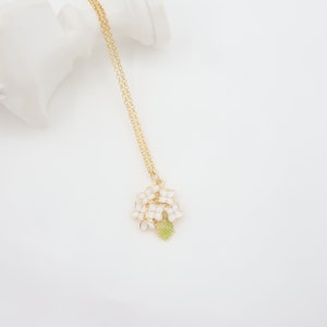 Peut inclure: Un collier en chaîne dorée avec un pendentif en forme de fleur en émail blanc. Le pendentif présente un groupe de petites fleurs blanches avec une feuille verte.