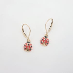 May include: A pair of gold ladybug earrings with red and black enamel. The earrings have a leverback closure.
