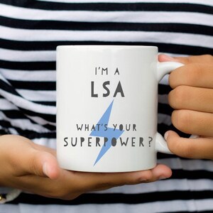 May include: White ceramic mug with a blue lightning bolt graphic and the text "I'm a LSA What's your superpower?"