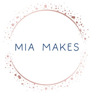 May include: A logo with the text "MIA MAKES" in navy blue, centered within a rose gold dotted circle on a white background. The rose gold circle has a textured, glittery appearance.