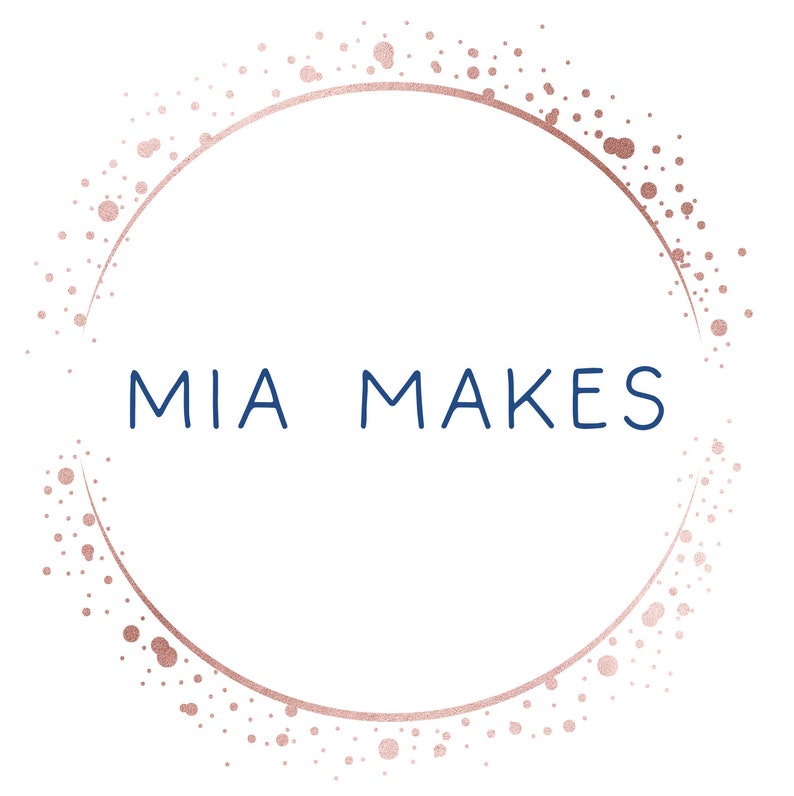 May include: A logo with the text "MIA MAKES" in navy blue, centered within a rose gold dotted circle on a white background. The rose gold circle has a textured, glittery appearance.