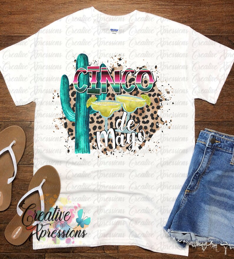 Pu&ograve; includere: Una maglietta bianca con un design grafico di un cactus, due bicchieri di margarita e il testo "Cinco de Mayo" in un font colorato e stratificato. Lo sfondo &egrave; un motivo di schizzi bianchi con una sovrapposizione di stampa leopardata.