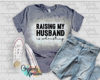 May include: A gray t-shirt with a white bleach design that says "Raising my husband is exhausting".