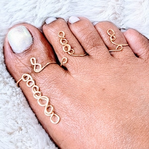May include: Gold toe rings with a delicate, looped design. The rings are worn on the big toe, second toe, and third toe.