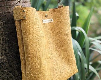May include: Mustard yellow shoulder bag with a floral embossed design. The bag has a matching adjustable strap and silver-tone hardware. The label reads "OMISY BAGS".