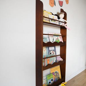 May include: A tall, dark wooden bookshelf with multiple shelves, filled with children's books and a doll. A garland of colorful fruit decorations hangs above. The bookshelf is approximately 60 inches tall.