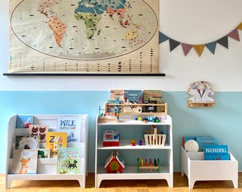 May include: A white bookshelf with a variety of children's books, including some with Polish titles. The bookshelf is in a room with a light blue wall and a world map hanging on the wall. There are also other toys and books on shelves in the room.