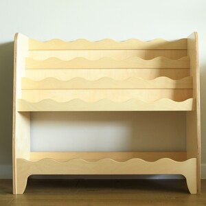 May include: A light wood bookshelf with wavy shelves. The bookshelf has two tiers and is designed to hold books or other items.