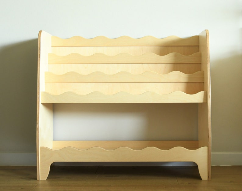 May include: A light wood bookshelf with wavy shelves. The bookshelf has two tiers and is designed to hold books or other items.