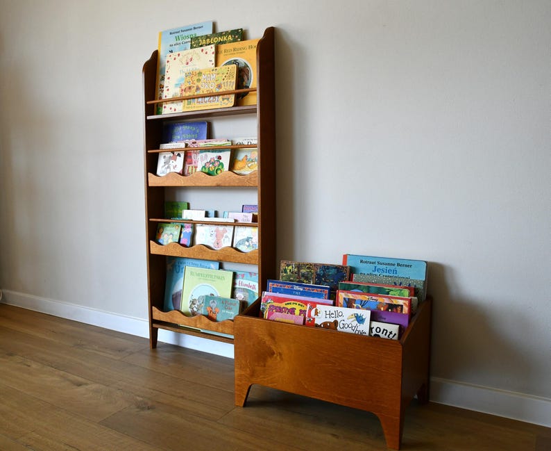 May include: Wooden bookshelf and a matching storage box filled with children's books. The bookshelf has multiple shelves with a scalloped edge design. The books are colorful and varied, suggesting a children's reading collection.