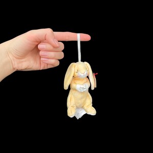 May include: A yellow plush bunny with a white belly and pink nose. The bunny is holding its paws together in a praying position. The bunny is hanging from a string.