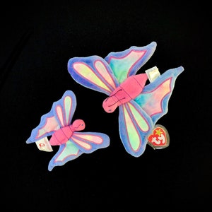 May include: Two plush butterfly toys, one larger than the other. The larger butterfly is purple, blue, and green with a pink body. The smaller butterfly is purple, blue, and pink. Both butterflies have a Ty tag.