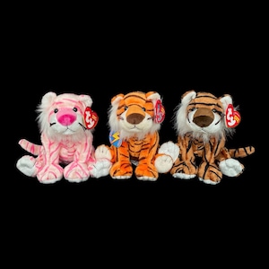 Puede incluir: Tres peluches de tigre Beanie Babies, una rosa, una naranja y una marrón, todas con una etiqueta roja y blanca.