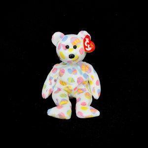 May include: White plush teddy bear with a colourful Easter egg pattern. The bear has a red Ty tag attached to its ear.