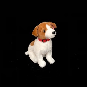 Może przedstawiać: Pluszowa zabawka przedstawiająca psa rasy Jack Russell Terrier. Pluszak jest biały z brązowymi plamami na głowie i uszach. Ma czerwoną obrożę i siedzi. Tło jest czarne.