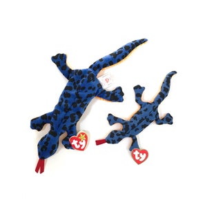 May include: Two blue and orange Ty Beanie Babies, a larger and a smaller version of a lizard with black spots. Both have a red Ty tag with a white star.