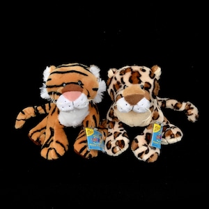 Peut inclure: Deux peluches : un tigre et un léopard. Le tigre a des rayures orange et noires, des détails blancs et un nez rose. Le léopard a un motif tacheté beige et marron. Les deux ont des étiquettes attachées.