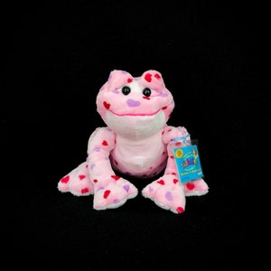 May include: Pink frog plush toy with red and purple hearts all over. The toy has a Webkinz tag attached to it.