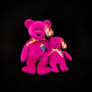 Puede incluir: Dos osos de peluche magenta con ojos negros y etiquetas rojas. El oso más grande tiene una cinta dorada y un parche de sol y globo. El oso más pequeño tiene un diseño similar. Ambos osos están sobre un fondo negro.