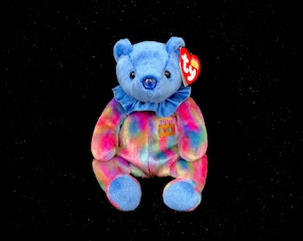 May include: A blue and rainbow tie-dye Beanie Baby teddy bear with a red Ty heart tag that says "Ty" and a birthday cake graphic on its chest.