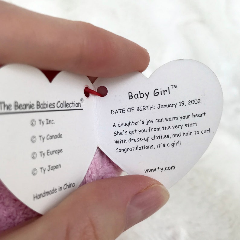 May include: Pink heart-shaped Beanie Baby tag with the words "Baby Girl" and "Date of Birth: January 19, 2002". The tag also includes the text "A daughter's joy can warm your heart. She's got you from the very start. With dress-up clothes, and hair to curl. Congratulations, it's a girl!" and "www.ty.com".