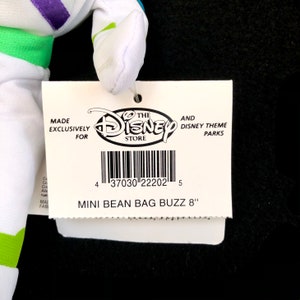 May include: A white and green Buzz Lightyear mini bean bag plush toy with a tag that reads "The Disney Store" and "Mini Bean Bag Buzz 8". The tag also includes a barcode and the text "Made exclusively for".