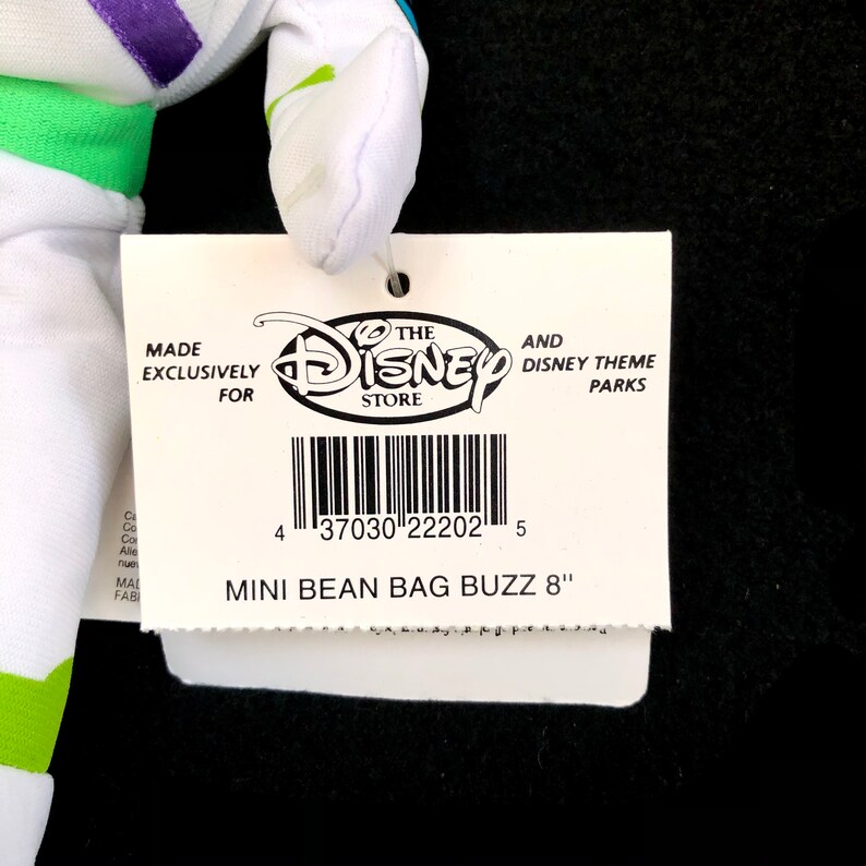 May include: A white and green Buzz Lightyear mini bean bag plush toy with a tag that reads "The Disney Store" and "Mini Bean Bag Buzz 8". The tag also includes a barcode and the text "Made exclusively for".