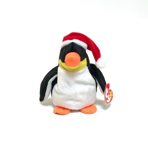 Peut inclure: Un jouet en peluche de pingouin noir et blanc portant un bonnet de Père Noël rouge. Le pingouin a un bec jaune et des pieds orange. Le jouet a une étiquette Ty rouge et blanche attachée à lui.