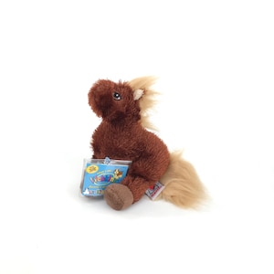 May include: A brown plush horse with a tan mane and tail. The stuffed animal has a tag that reads "Webkinz". The horse is sitting on a white surface.