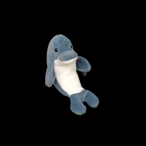 Puede incluir: Un juguete de peluche de delfín azul y blanco. El delfín está acostado de lado con la cola enroscada.