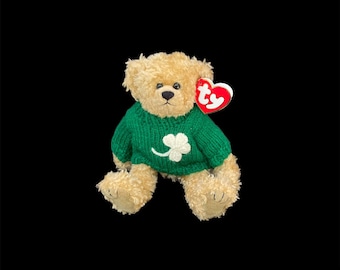 Peut inclure: Un ours en peluche brun portant un pull vert avec un trèfle à quatre feuilles blanc. L'ours a une étiquette Ty rouge attachée à son oreille.