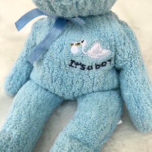 May include: A light blue plush teddy bear with a white swan and the text "It's a boy" embroidered on the chest. The bear has a blue ribbon around its neck.
